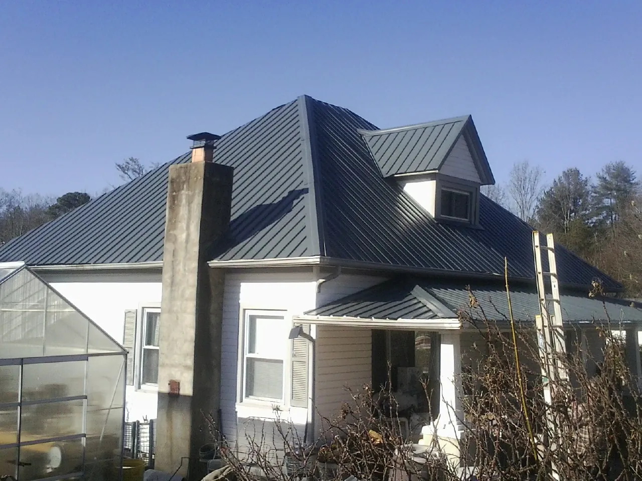 Dark blue standing seam metal roof on a white farmhouse with dormer — Slate & Tile Roof Repair by Roofing Brothers in Tome