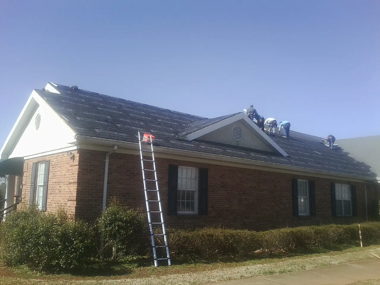 Crew tearing shingles off a brick ranch roof with a ladder set — Emergency Roof Repair work by our crew in Tome