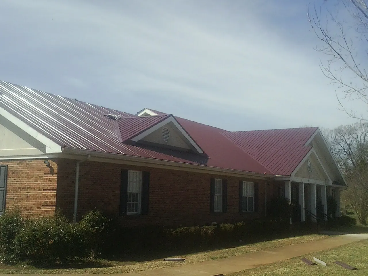 Red metal roof with gabled entries on a long brick building, from a Hail Damage Roof Repair job in Tome