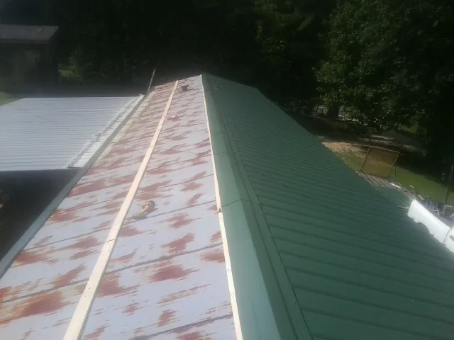Old rusted panels beside newly installed green metal roofing — Wind Damage Roof Repair by Roofing Brothers in Tome