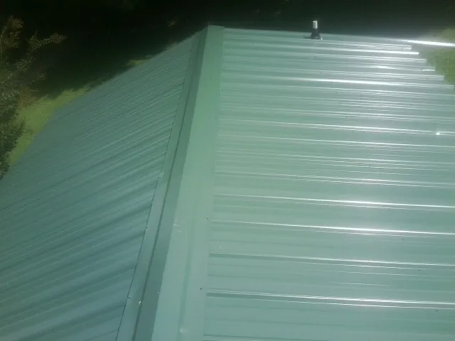 New green metal panels meeting at the ridge of a roof — Flat Roof Repair work by our crew in Tome