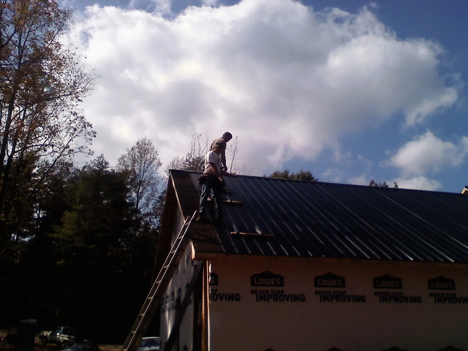 Roofer fastening dark metal panels high against a cloudy sky, from a Roof Inspection job in Tome